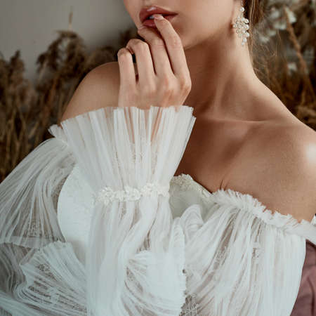 Beautiful woman hands with french manicure on a white wedding dress. Wedding morning of a young...