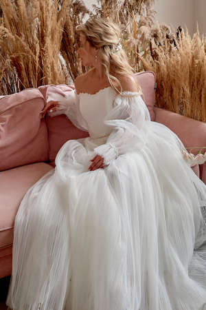 The bride in profile on a beautiful pink sofa. A room decorated with cereals. Luxury dress.の写真素材