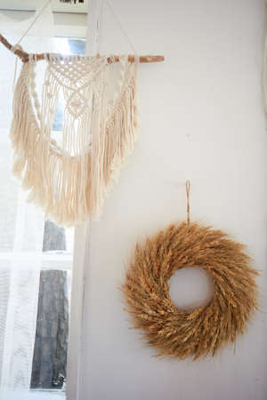 Decoration of the wall in the village house macrame and a wreath of cereals. Interior in boho style.