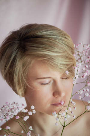 Portrait of a girl on a pink background with flowers. Tenderness and feminine. The sphere of beauty and womens health. Short haircut, blonde hairの写真素材