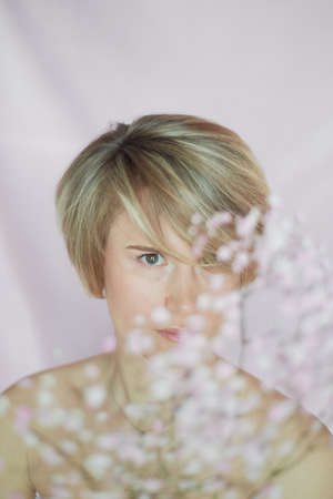 Portrait of a girl on a pink background with flowers. Tenderness and feminine. The sphere of beauty and womens health. Short haircut, blonde hairの写真素材