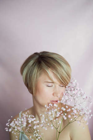 Portrait of a girl on a pink background with flowers. Tenderness and feminine. The sphere of beauty and womens health. Short haircut, blonde hairの写真素材