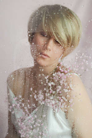 Portrait of a girl on a pink background with flowers. Tenderness and feminine. The sphere of beauty and womens health. Short haircut, blonde hairの写真素材