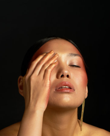 An Asian girl on a black background in the studio. Gold. The emotion of fatigue and disappointmentの写真素材