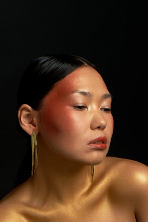 An Asian girl on a black background in the studio. Gold. Thin collarbones. Long gold earrings. The realm of beauty and perfumeの写真素材
