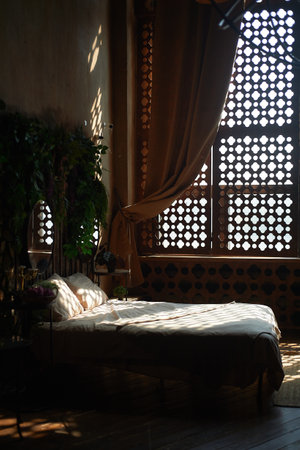 Bed with plain linen, with spots of light from the blinds. Cozy boho style bedroomの写真素材