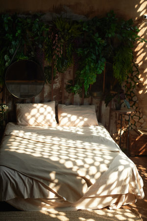 Bed with plain linen, with spots of light from the blinds. Cozy boho style bedroomの写真素材