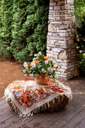 Wedding decoration in the Slavic style. Birch bark box with a flower arrangement in orange with ranunculi and greenery. Hay and a painted shawlの写真素材