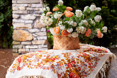 Wedding decoration in the Slavic style. Birch bark box with a flower arrangement in orange with ranunculi and greenery. Hay and a painted shawlの写真素材