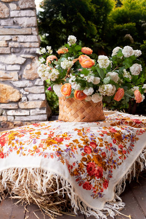 Wedding decoration in the Slavic style. Birch bark box with a flower arrangement in orange with ranunculi and greenery. Hay and a painted shawlの写真素材