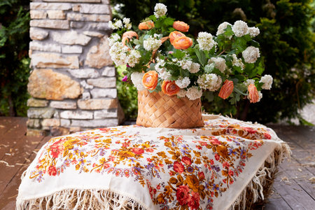 Wedding decoration in the Slavic style. Birch bark box with a flower arrangement in orange with ranunculi and greenery. Hay and a painted shawlの写真素材