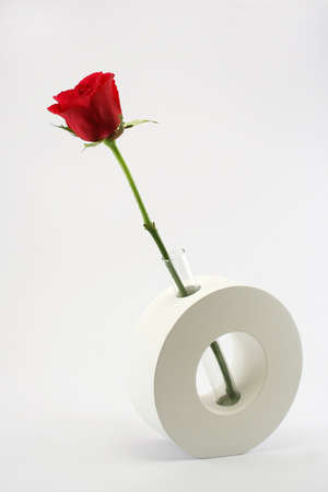 A single long stemmed red rose in a modern glass and ceramic vase against a neutral backgroundの写真素材