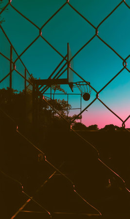 Silhouette of fence and basketball net with sunset sky background.