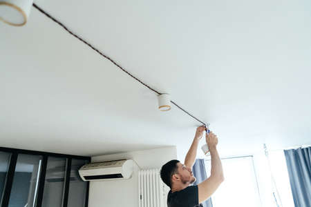 man with a screwdriver in his hands fastens a lamp on the ceiling in his light house. repair and improvement.の写真素材