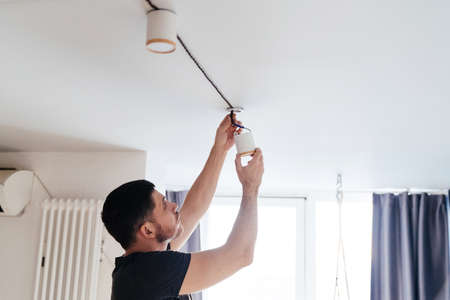 man in a gray t-shirt fastens a lamp on the ceiling in his light house. repair and improvement.の写真素材