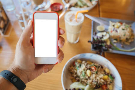 mockup of a samrtphone in the hand of a white man in red frames, against the background of a cafe and a table with foodの写真素材