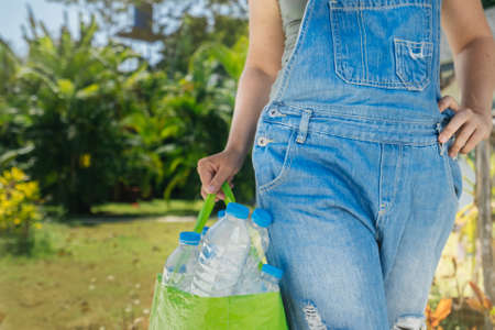 Plastic collection, environmental protection. Transparent plastic bottles in a bag. Female hand with a full bag for recycling on a background of tropical greenery.の写真素材