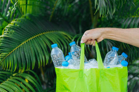 Bag with plastic bottles in a man's hand against the background of tropical summer greenery. Plastic collection, environmental protection.の写真素材