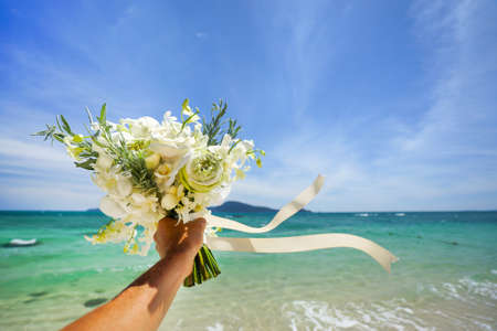 Wedding bouquet of white flowers in hand . Against the background of blue sea and tropical islands .の写真素材