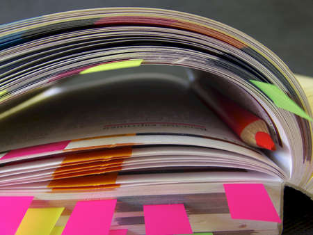 Book with a lot of bookmarks in its pages and a red pencil used as a bookmark.の写真素材