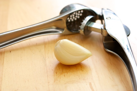 Garlic masher lies on a wooden table next to the garlic clove.の写真素材