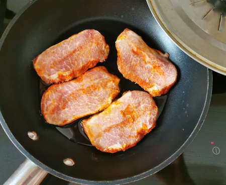 pieces of pork meat in a frying pan with a lid on the stoveの写真素材
