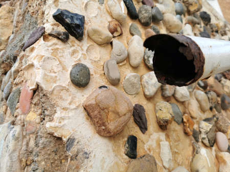 rusty broken pipe against a wall of cement, sand and stones