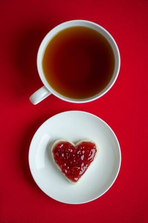 A cup of tea and a sandwich in the shape of a heart with raspberry jamの写真素材