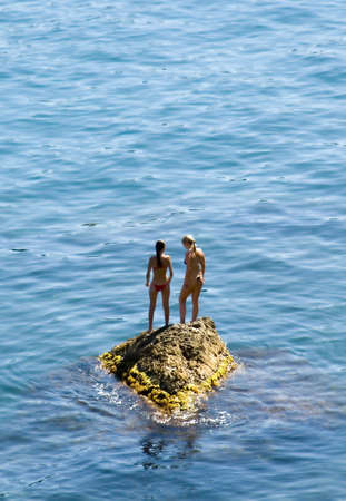 Two girls on a rock in the middle of picturesque oceanの写真素材
