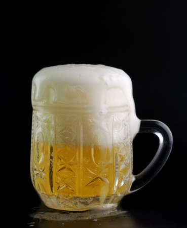 Glass of beer on a black background with the foam poured aroundの写真素材