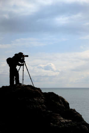 The photographer on mountain. A silhouette of the person with the camera on a background of the skyの写真素材