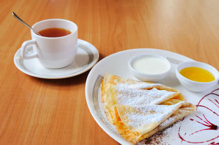 Tea and pancakes with powdered sugar. The dish is decorated by cowberry jamの写真素材