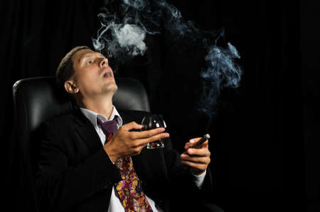 The man with a cigar and a glass of cognac. A dark backgroundの写真素材