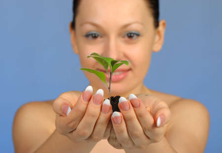 The woman holds in hands soil with a plant. Selective focus. A blue backgroundの写真素材