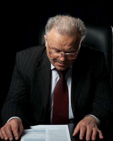 The elderly man in eyeglases reads the document. A photo against a dark backgroundの写真素材