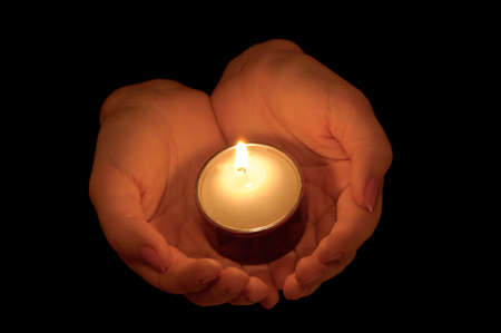 Burning candle in female hands. A black background