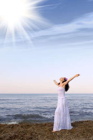 The woman in a white sundress on seacoast with open hands. Sun lightの写真素材