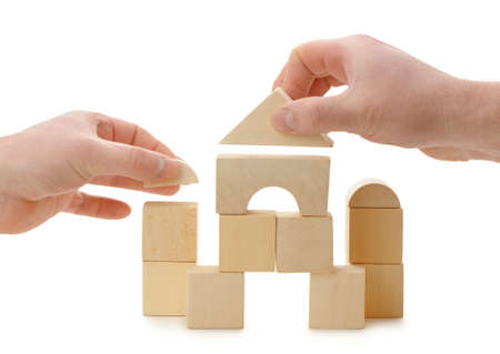 The hands establishes a toy roof on wooden cubes. Isolated on whiteの写真素材