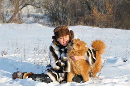 The woman in a mink fur coat plays with a dog. Winter weatherの写真素材