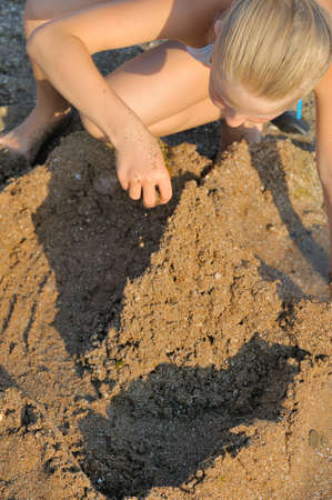 The girl builds sand castle. Sits on seacoastの写真素材