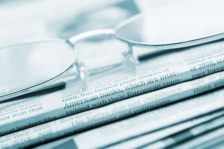 Eyeglasses lie on a pile of newspapers.Blue toned. A photo close up. Selective focusの写真素材