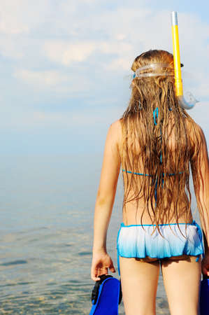 The girl on seacoast looks in a distance. In a mask, flippers and with a snorkelの写真素材