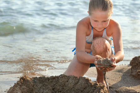 The girl builds sand castle. Sits on seacoastの写真素材