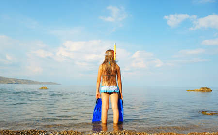 The girl on seacoast looks in a distance. In a mask, flippers and with a snorkelの写真素材