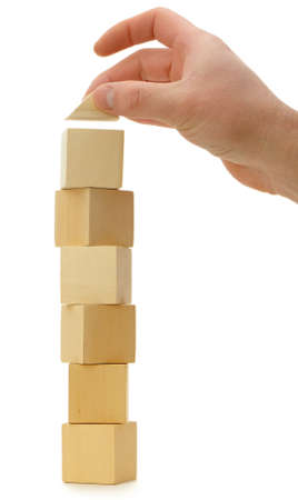 The hand establishes a toy roof on wooden cubes. Isolated on whiteの写真素材
