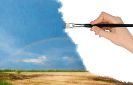 The hand with a brush draws a landscape.The blue sky, field and rainbowの写真素材