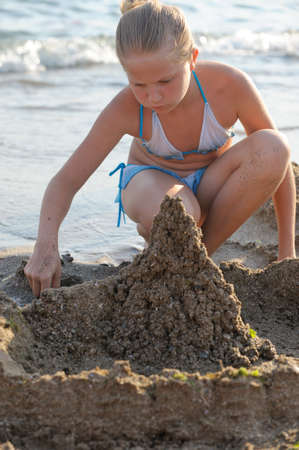 The girl builds sand castle. Sits on seacoastの写真素材
