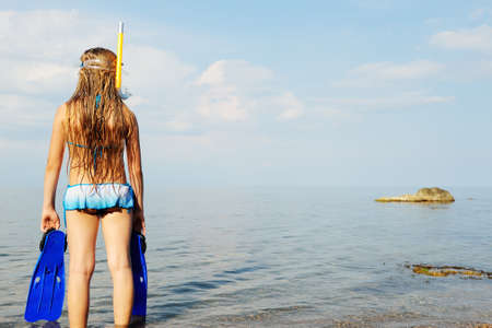 The girl on seacoast looks in a distance. In a mask, flippers and with a snorkelの写真素材