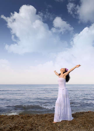 The woman in a white sundress on seacoast with open hands. Cloud skyの写真素材