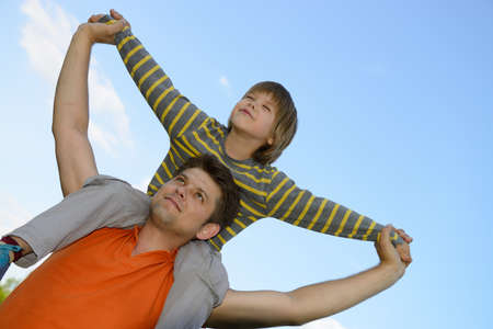 Happy son on the shoulders of the father. On the background of blue skyの写真素材